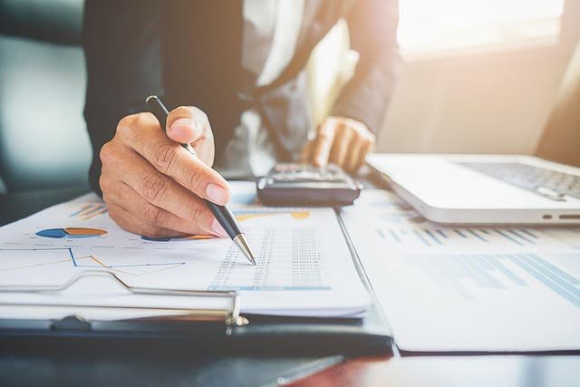 Businessman analyzing financial charts with calculator and documents at a desk in Burnaby