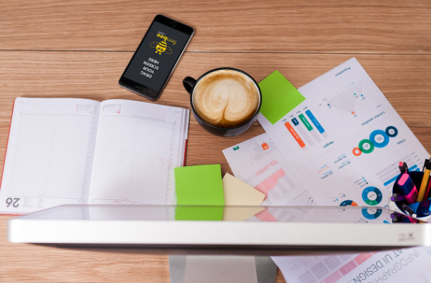 Business reports, financial charts, notebook, coffee cup, and smartphone on a desk, representing audit and review engagement planning for Canadian businesses.